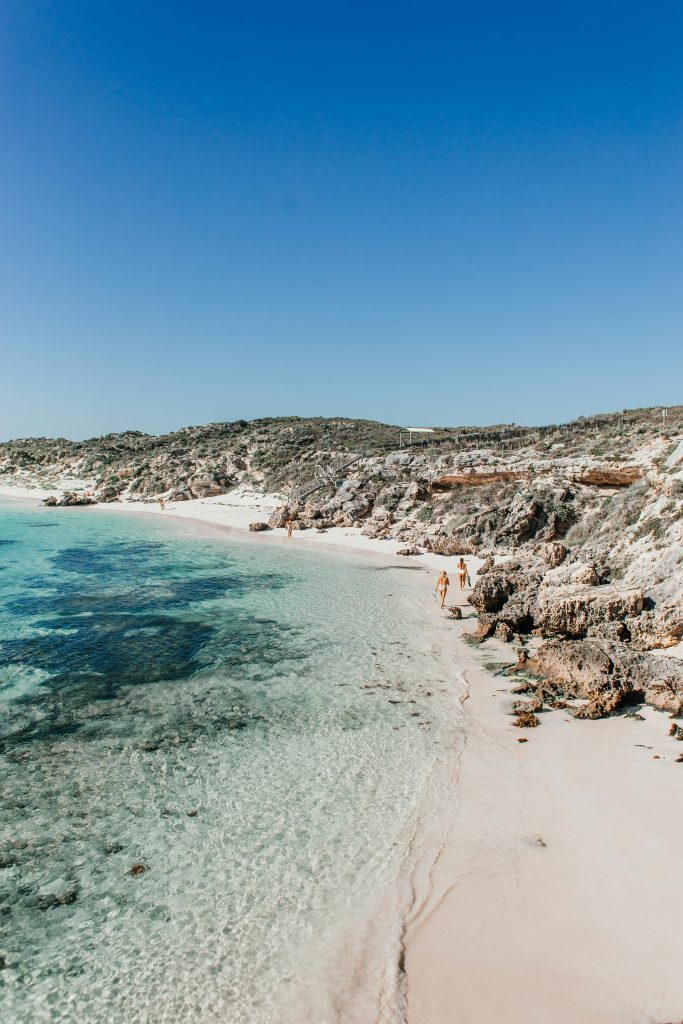 Stunning beach scene with clear water, rocky shoreline, and a bright blue sky.
